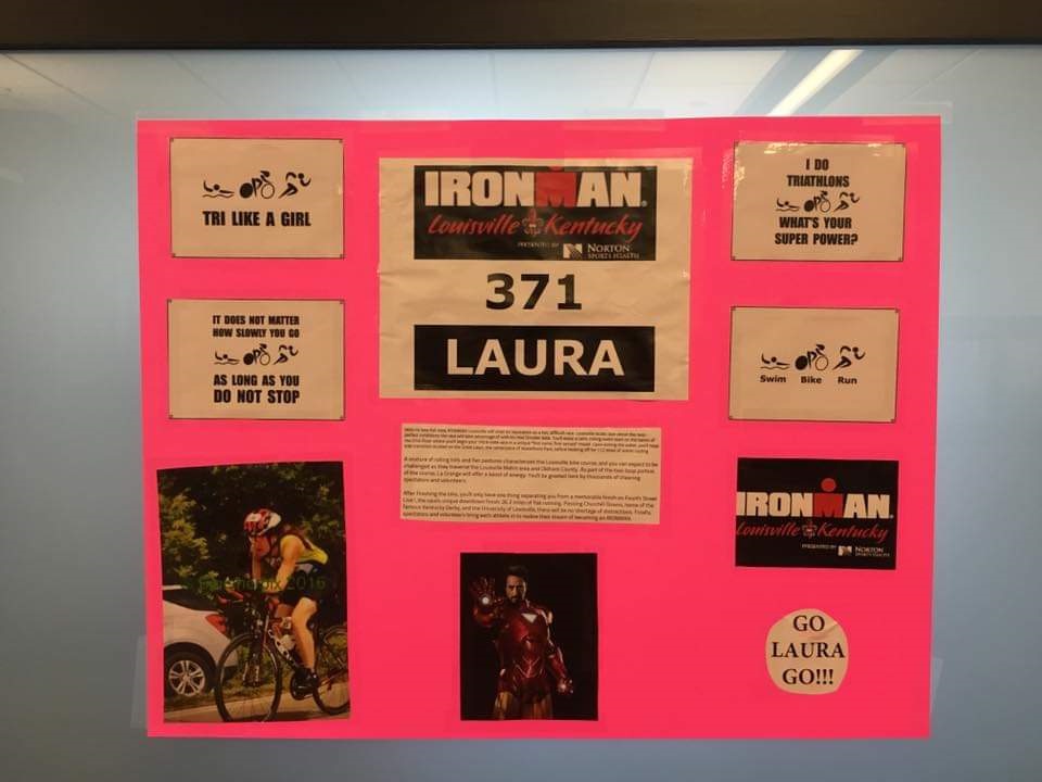 A neon pink sign with Laura's Ironman participant number, photos, and notes of encouragement from the marathon