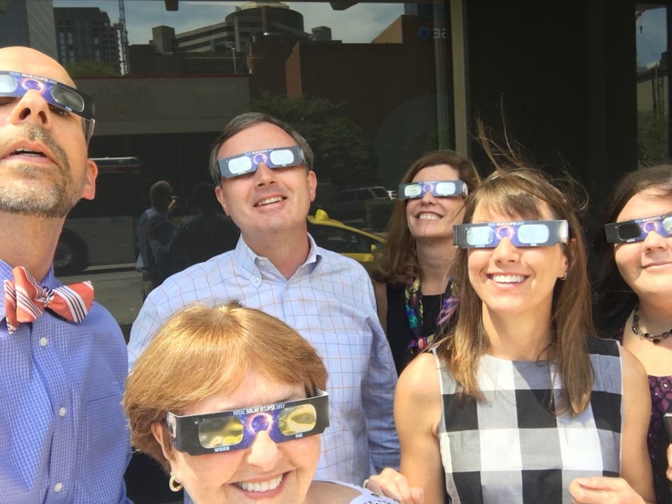 Laura and teammates stand outside the office and view the solar eclipse with special glasses