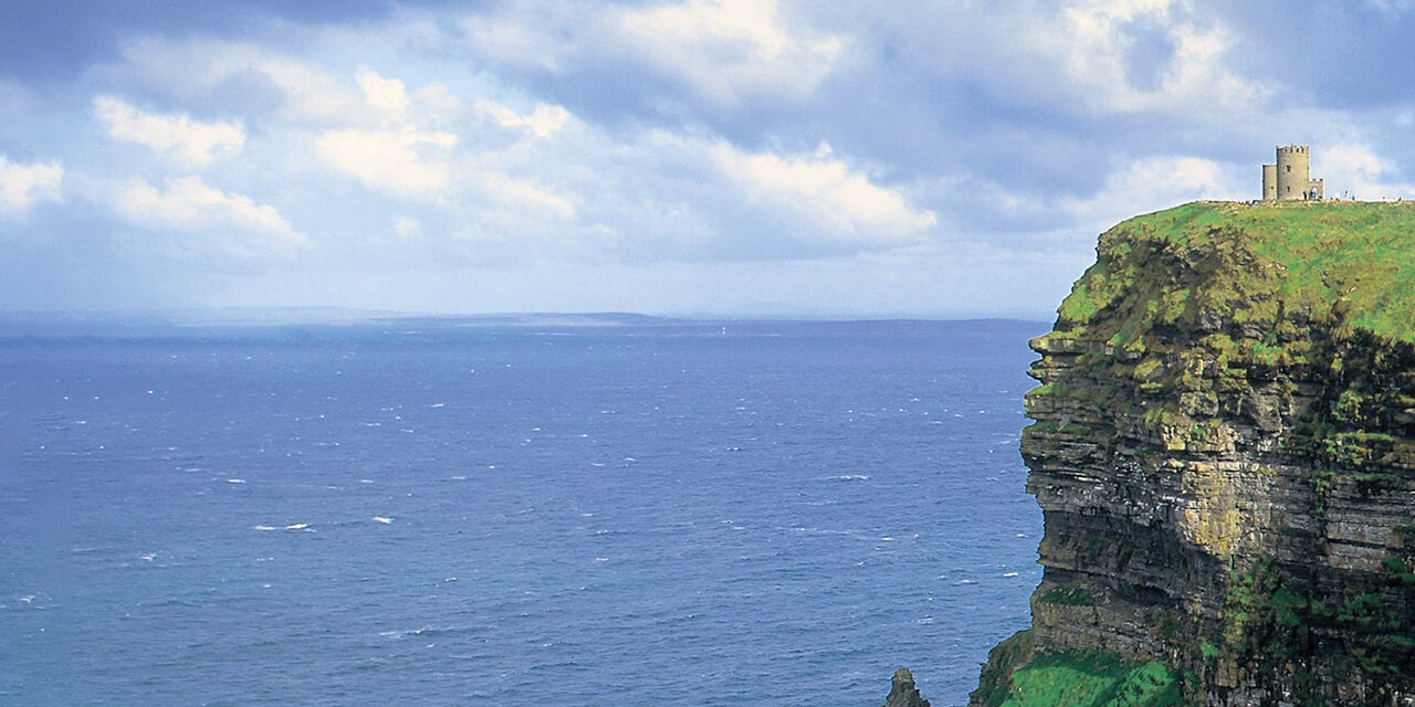 Landscape image of a stone castle on top of a cliff overlooking the sea