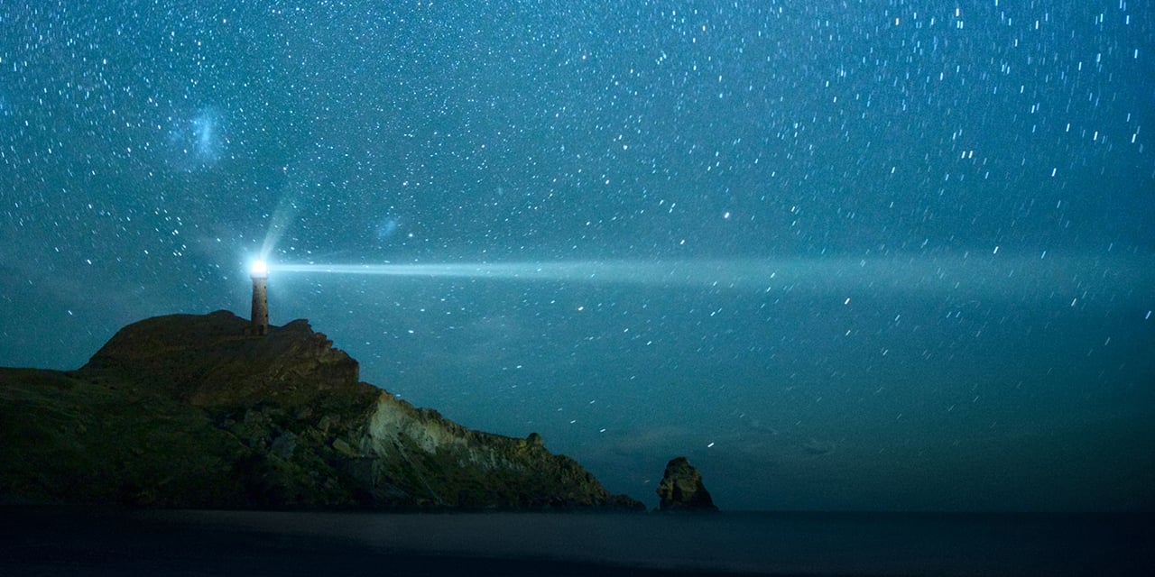 Lighthouse on top of a hill at night. 