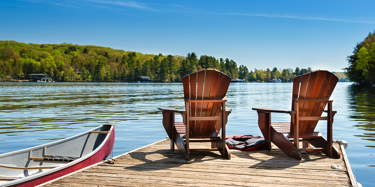 A lakeside dock with two wooden chairs and a canoe under clear skies, suggesting relaxation and long‑term planning.