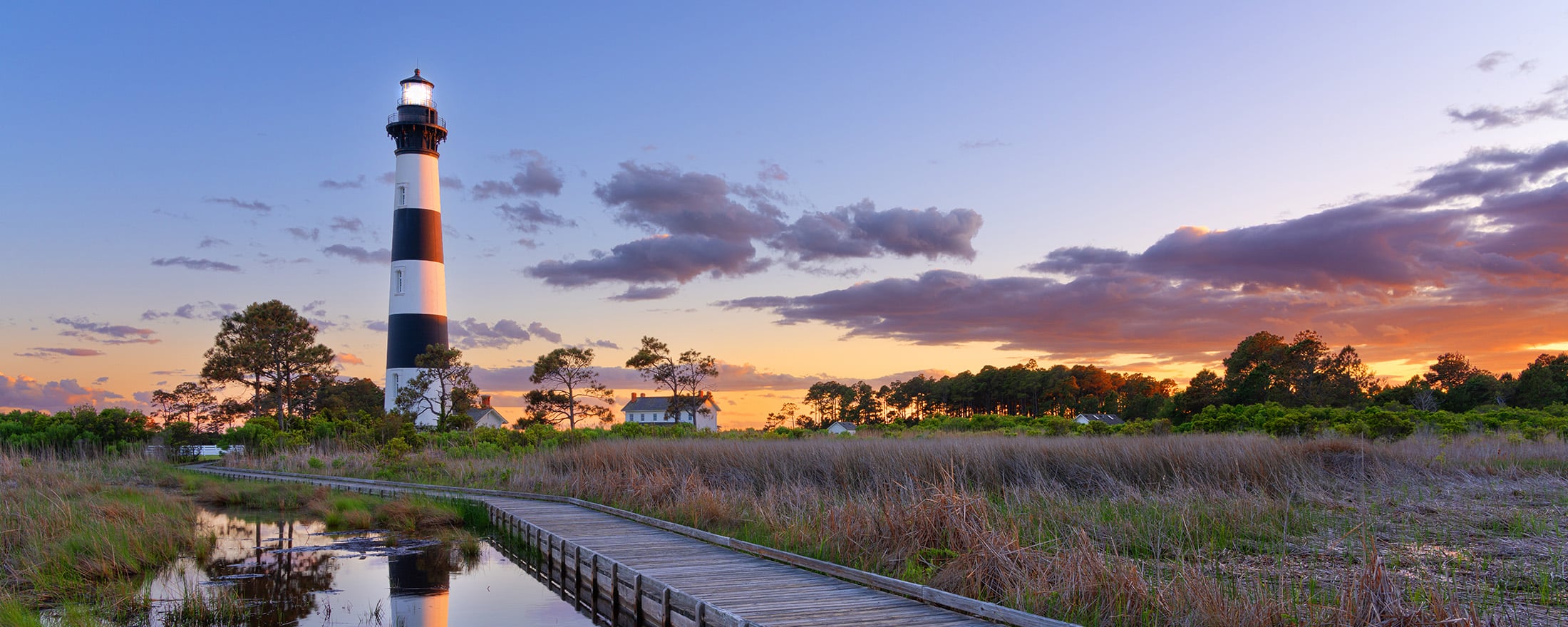 A pier over water leading up to a lighthouse at dusk