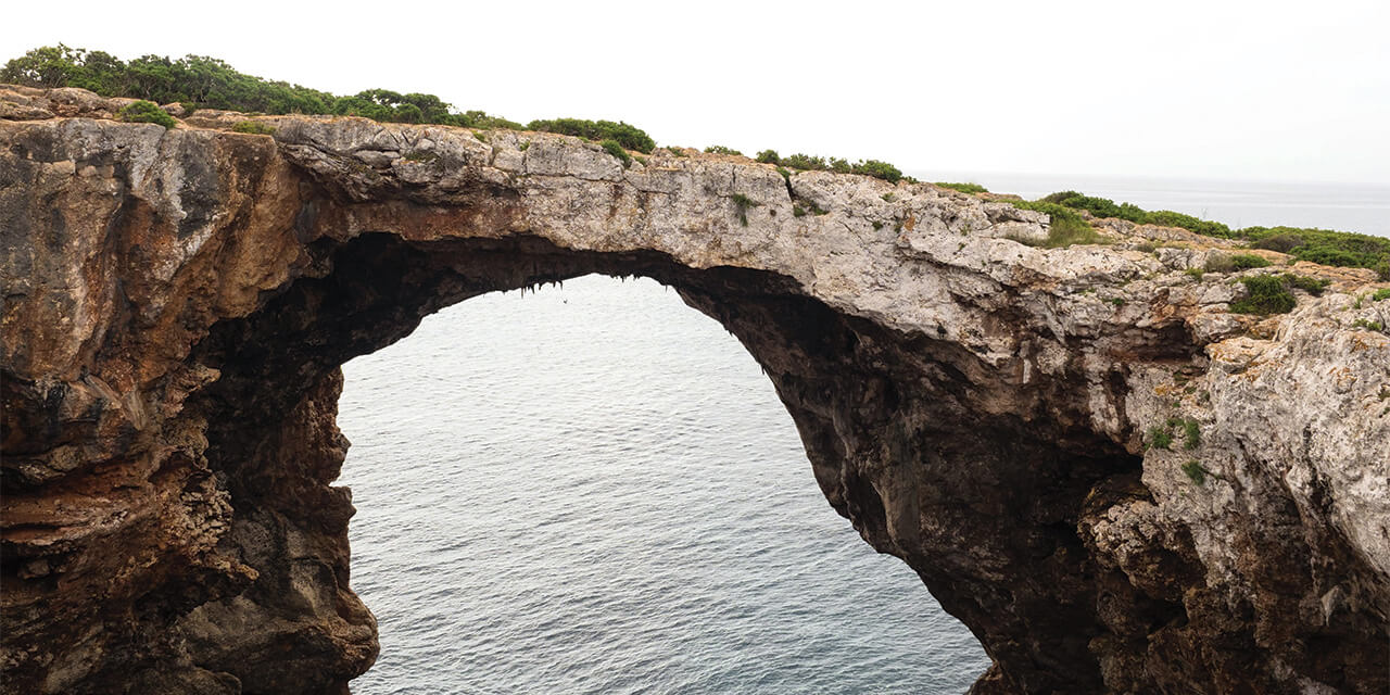 A natural bridge formed by a rock formation over water against a hazy gray sky