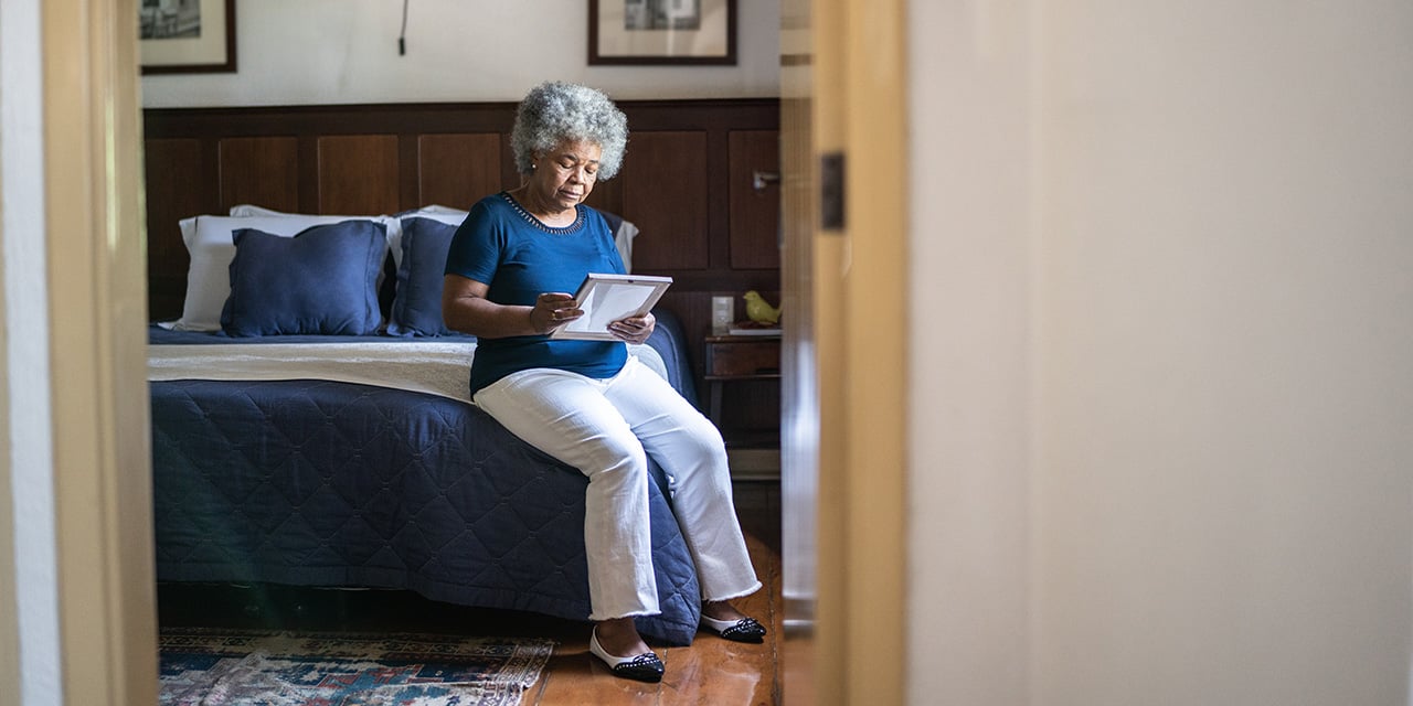 Woman sitting along on edge of bed looking at a photograph.