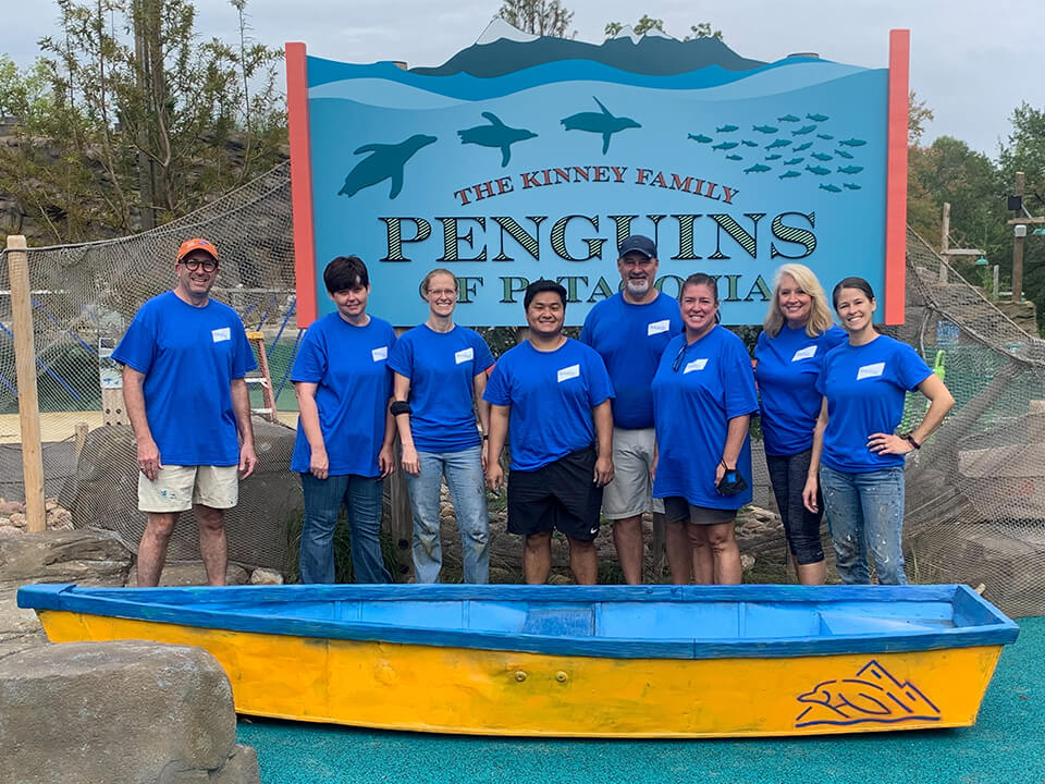 Baird Trust associates volunteer group standing outside of the Kinney Family Penguins of Patagonia sign