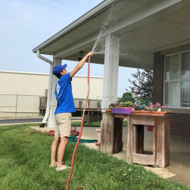 An associate wearing a Baird Gives Back t-shirt cleans the exterior of a house with a hose