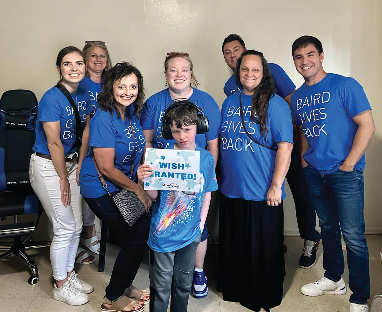 A group of Baird associates with a young child wearing gaming headphones holding a sign that reads, "Wish Granted!"