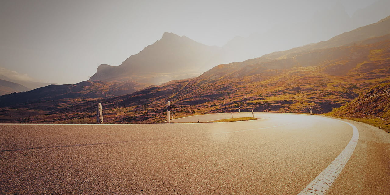 A road curving off into the mountains as the sun rises over them