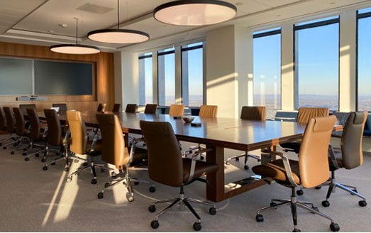 Wide, angled photo of a modern conference room with 18 high-backed desk chairs around a long table