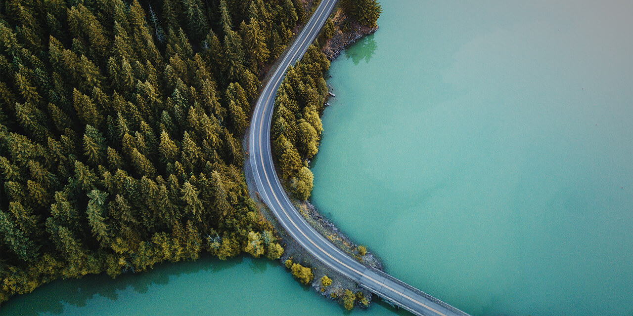 Overhead image of a road winding through a forest and into a bridge over water