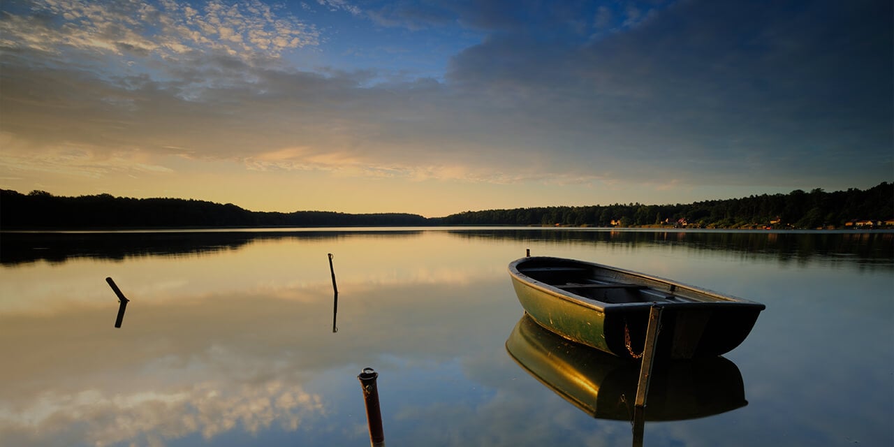 Image of an empty rowboat floating on a still lake at dusk.