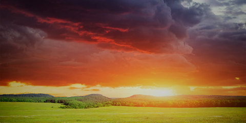 Landscape photo of a field with a stormy sky rolling away from a sunset